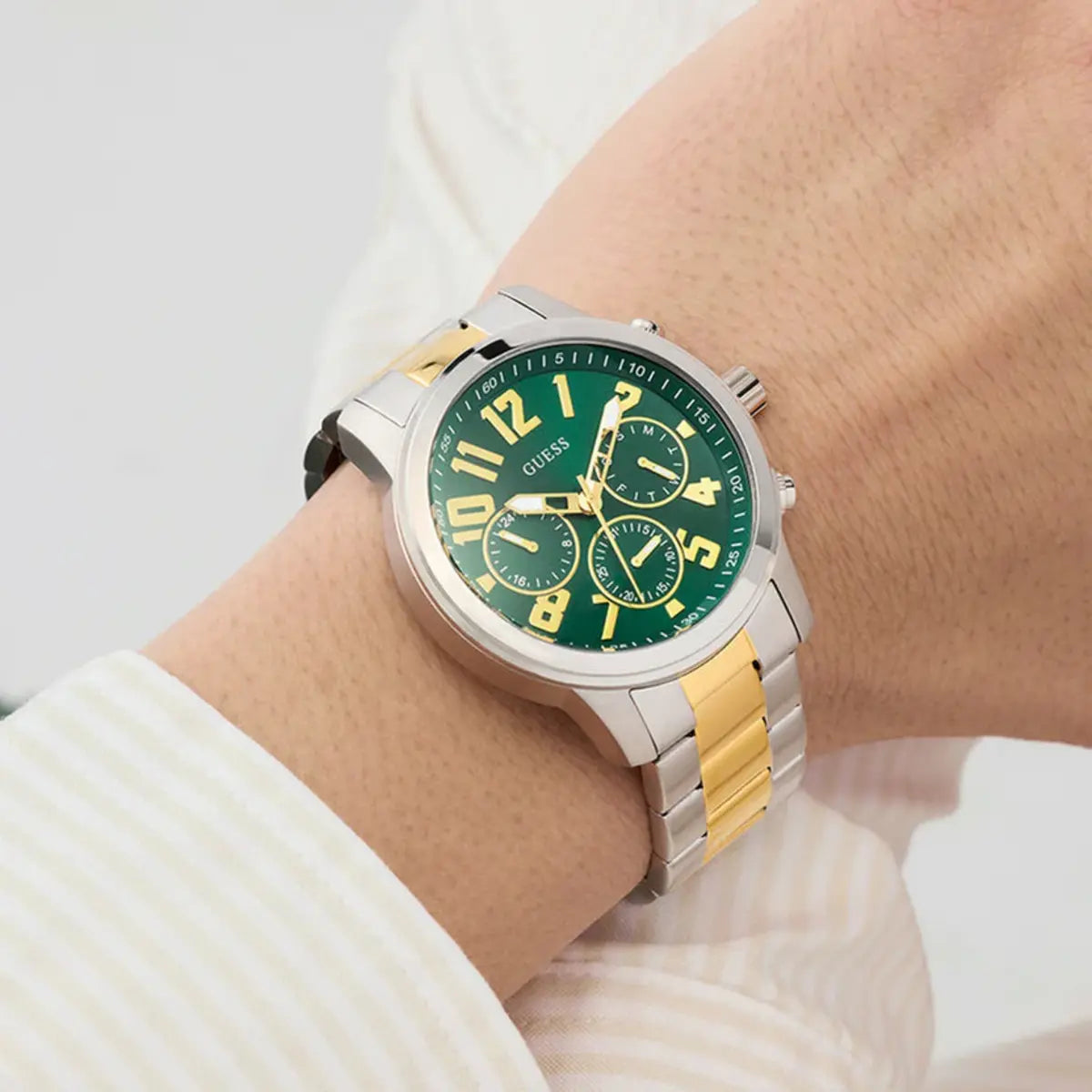 Green watch with gold and silver accents on a wrist, brand 'GUESS' visible
