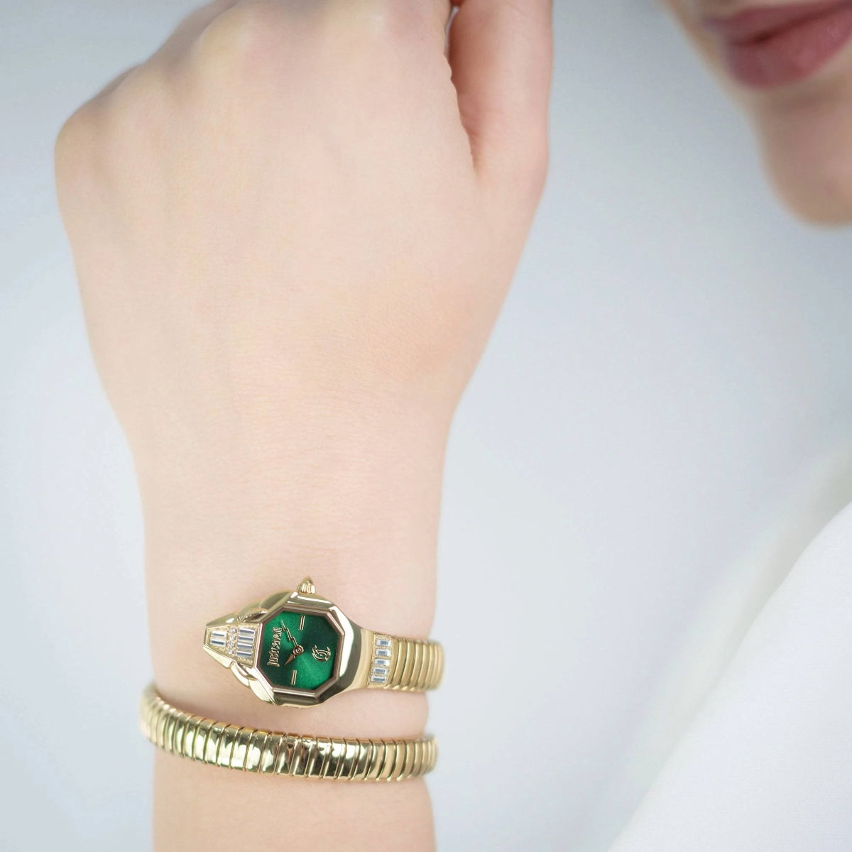 Gold watch with green face on a wrist against a light background