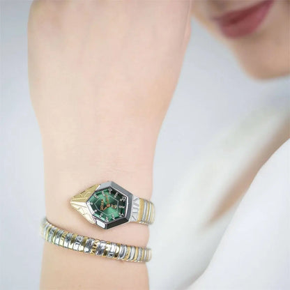 Close-up of a wrist wearing a gold and green hexagonal ring on a plain background