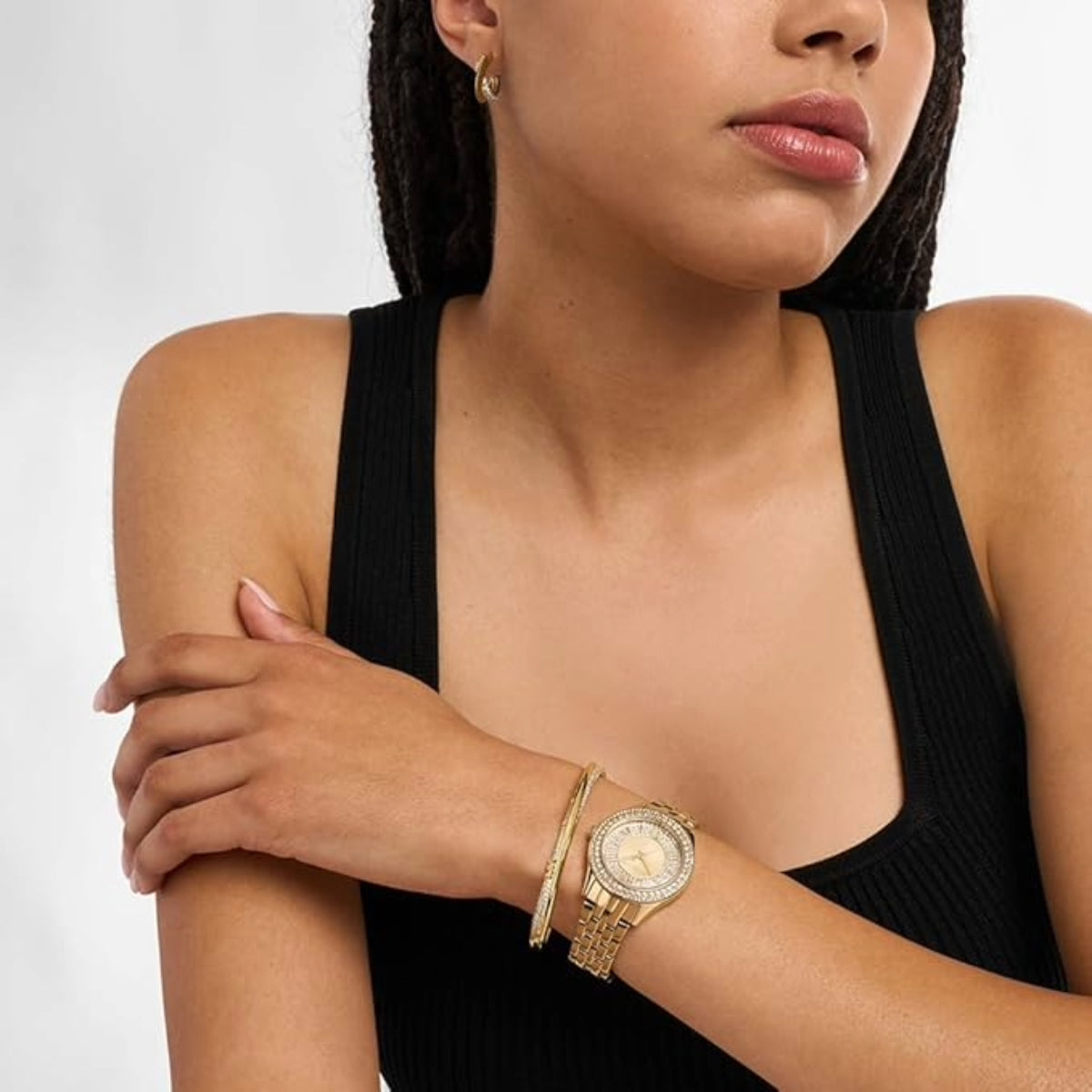 Woman wearing a gold watch and bracelet on a plain background
