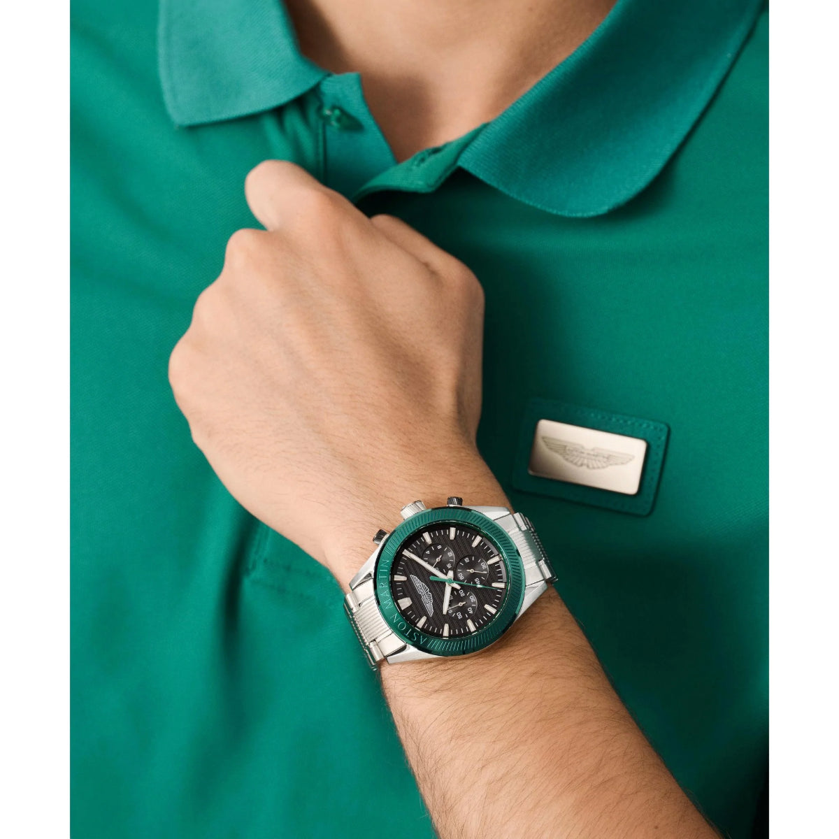Person wearing a green shirt with a brand logo and a green watch on a white background