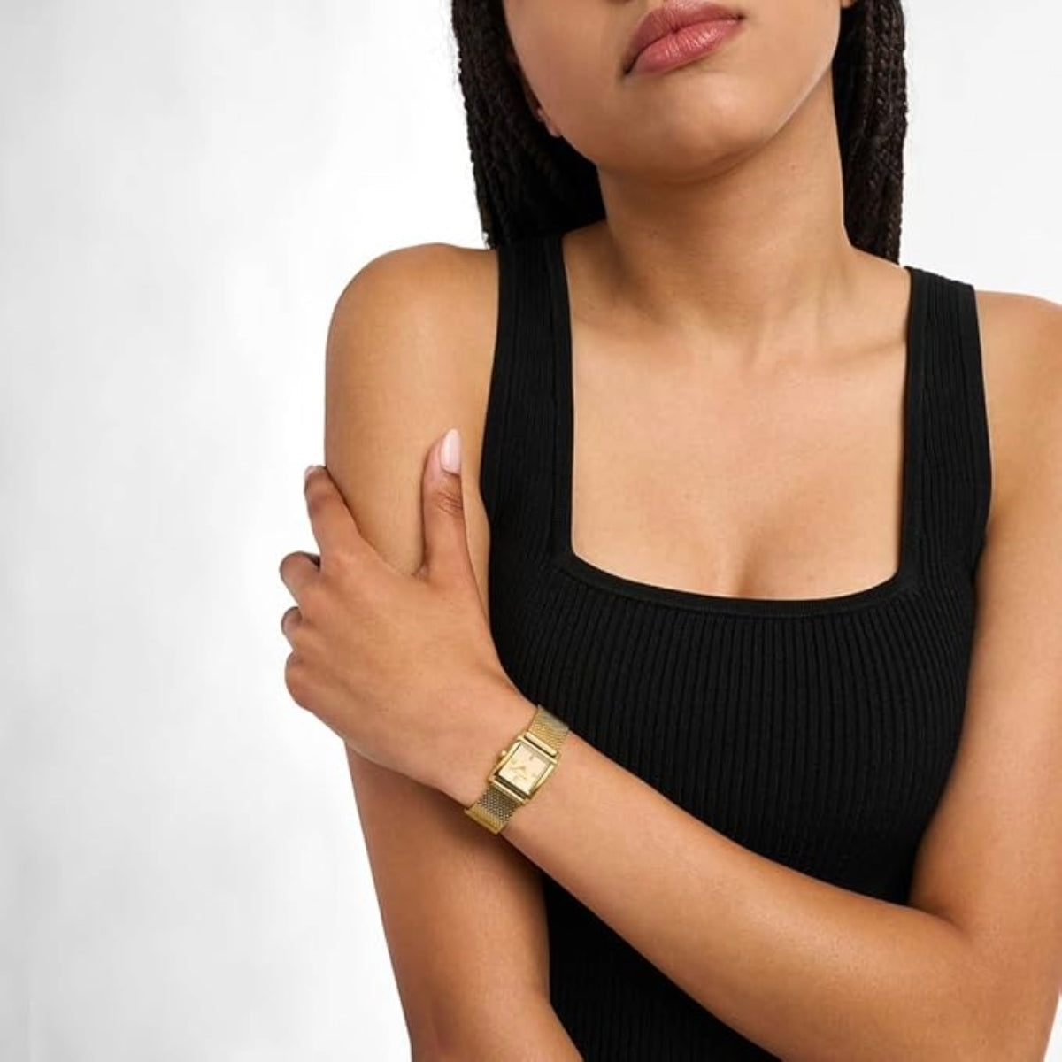 Woman wearing a black sleeveless top and gold watch on a white background