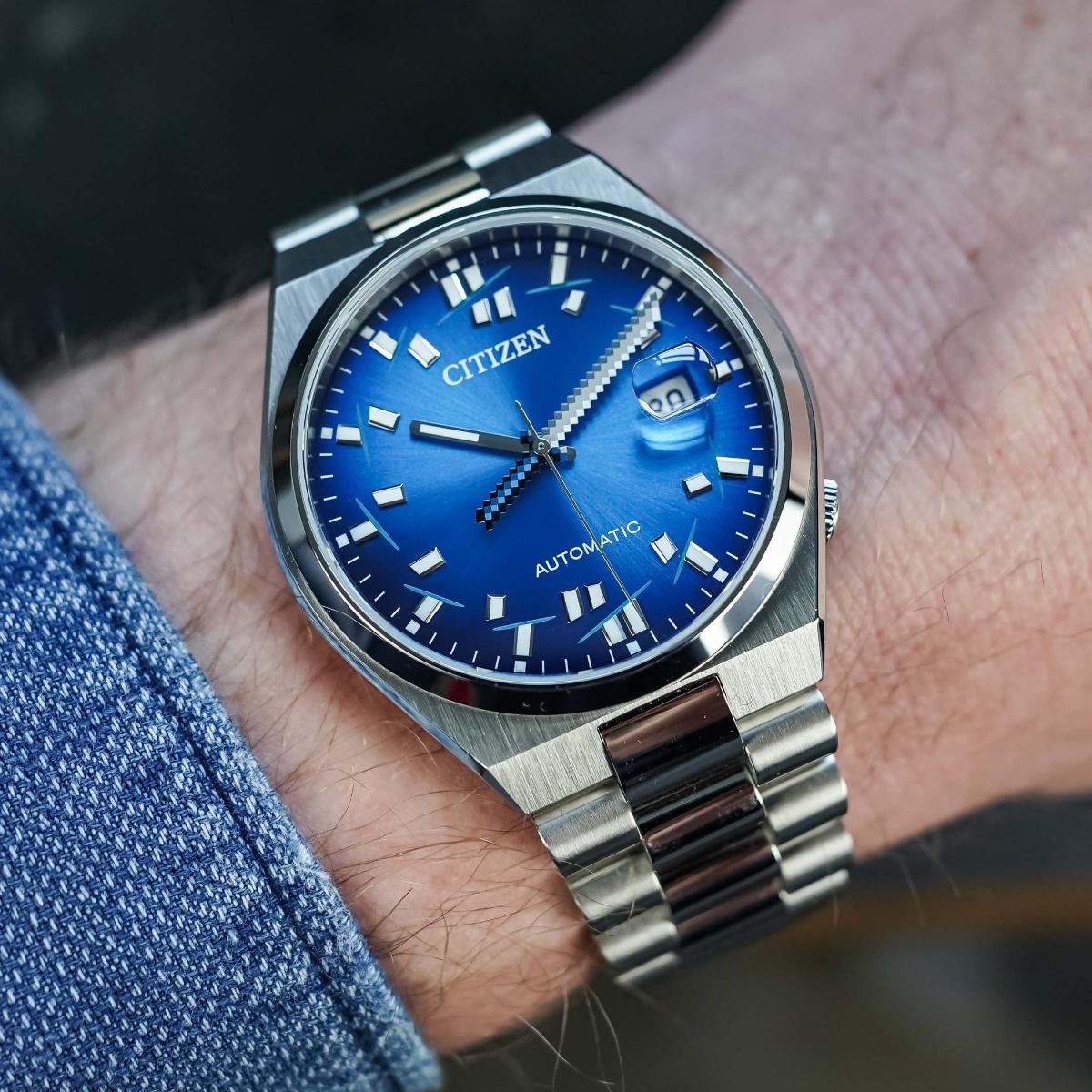 Silver Citizen watch with a blue dial on a wrist, worn with a denim sleeve.