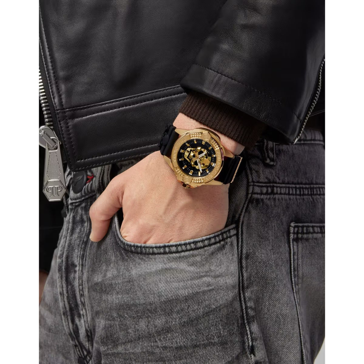 Gold watch on a wrist with a black leather strap, worn with a black jacket and gray jeans.