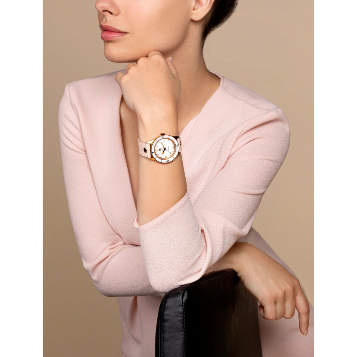 Woman wearing a pink sweater and gold watch on a beige background