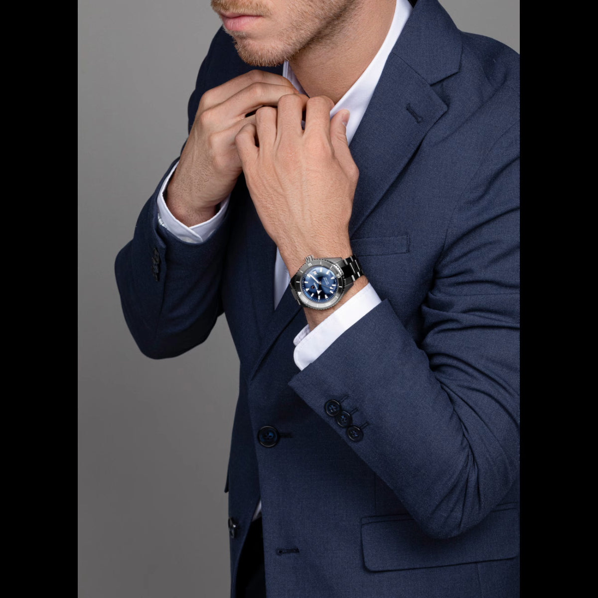 Man adjusting his tie wearing a navy suit with a gray background