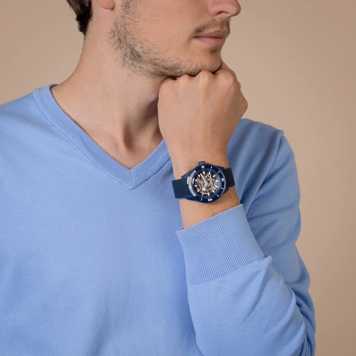 Man wearing a blue sweater and a watch with a beige background