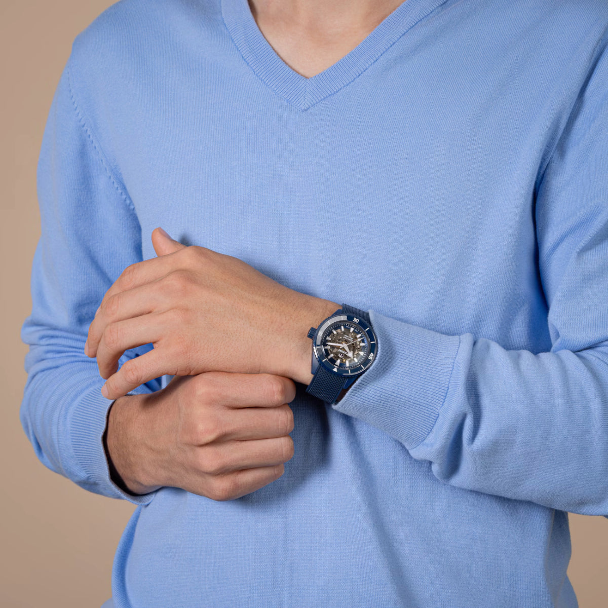 Person wearing a blue sweater with a watch on a beige background