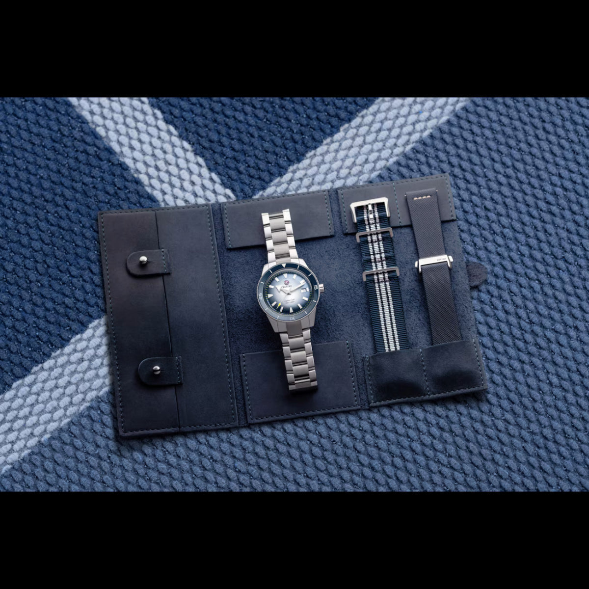 Watch set with silver watch and black straps on a textured blue surface