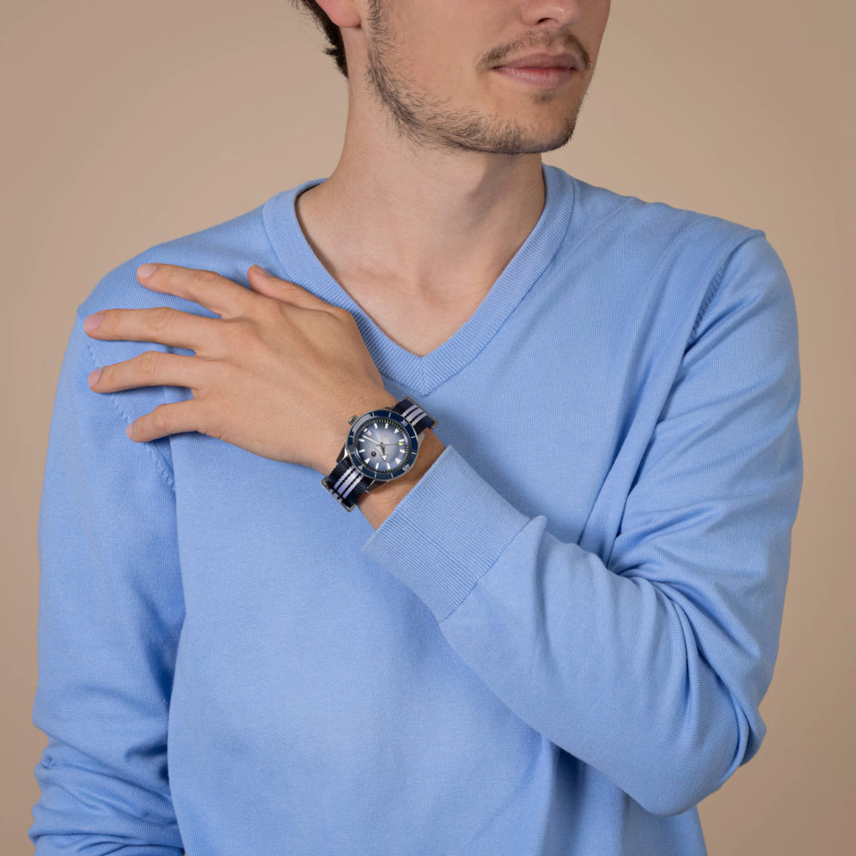 Man wearing a light blue long-sleeve shirt with a watch on his wrist against a beige background