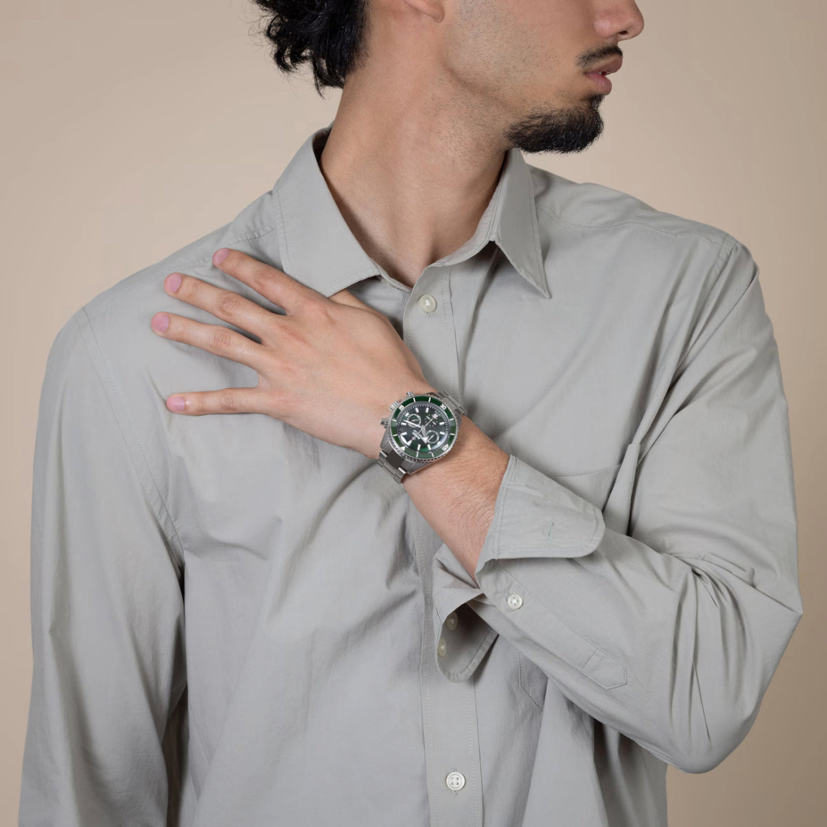 Man wearing a light gray shirt with a watch on his wrist, against a beige background