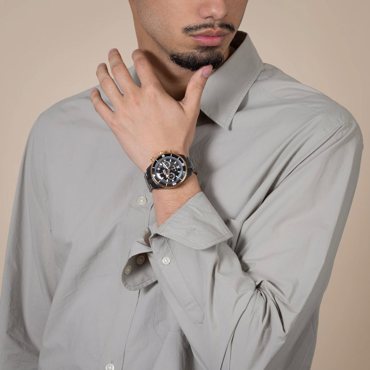 Man wearing a gray shirt with a watch on his wrist against a beige background