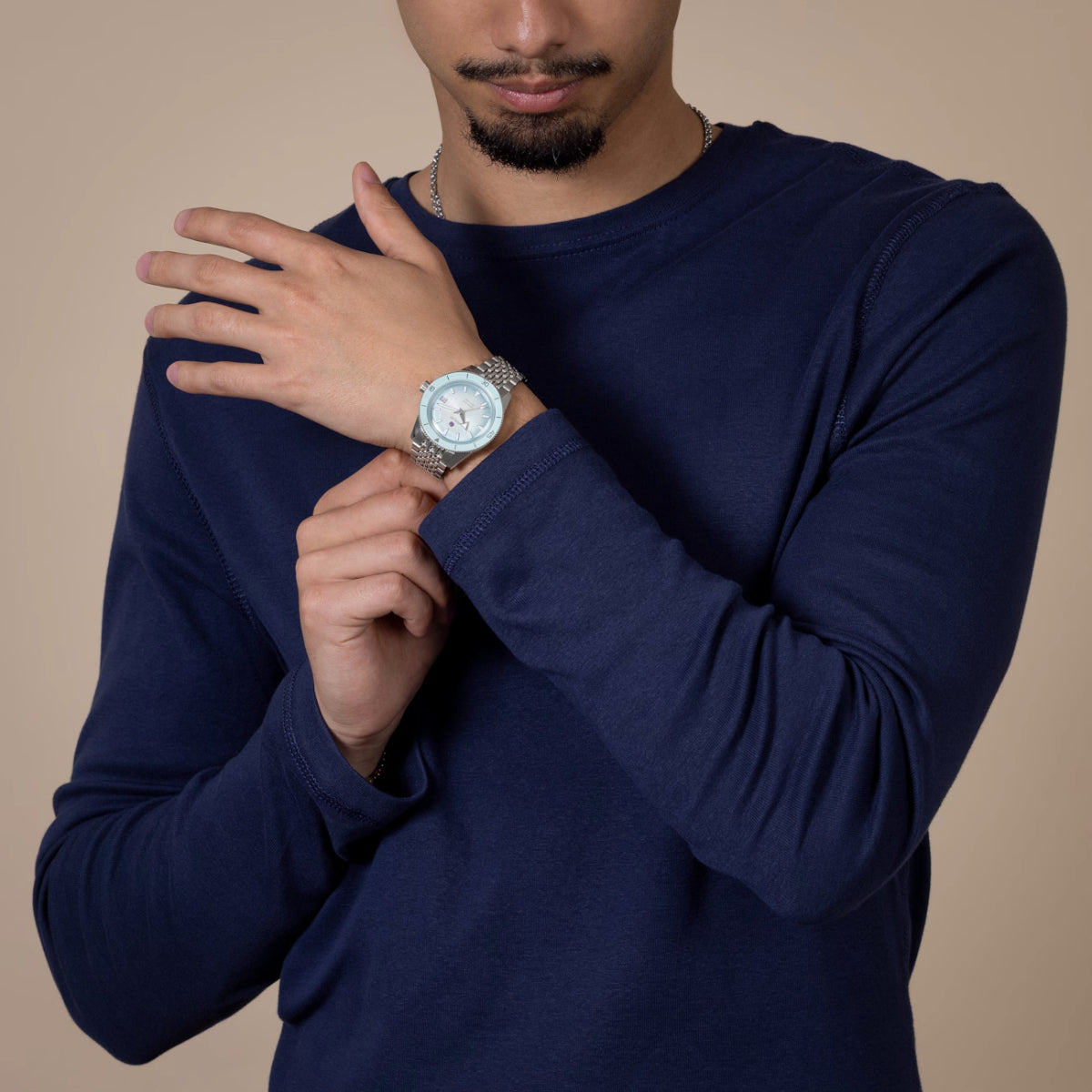 Man wearing a navy blue long-sleeve shirt with a watch on his wrist against a beige background