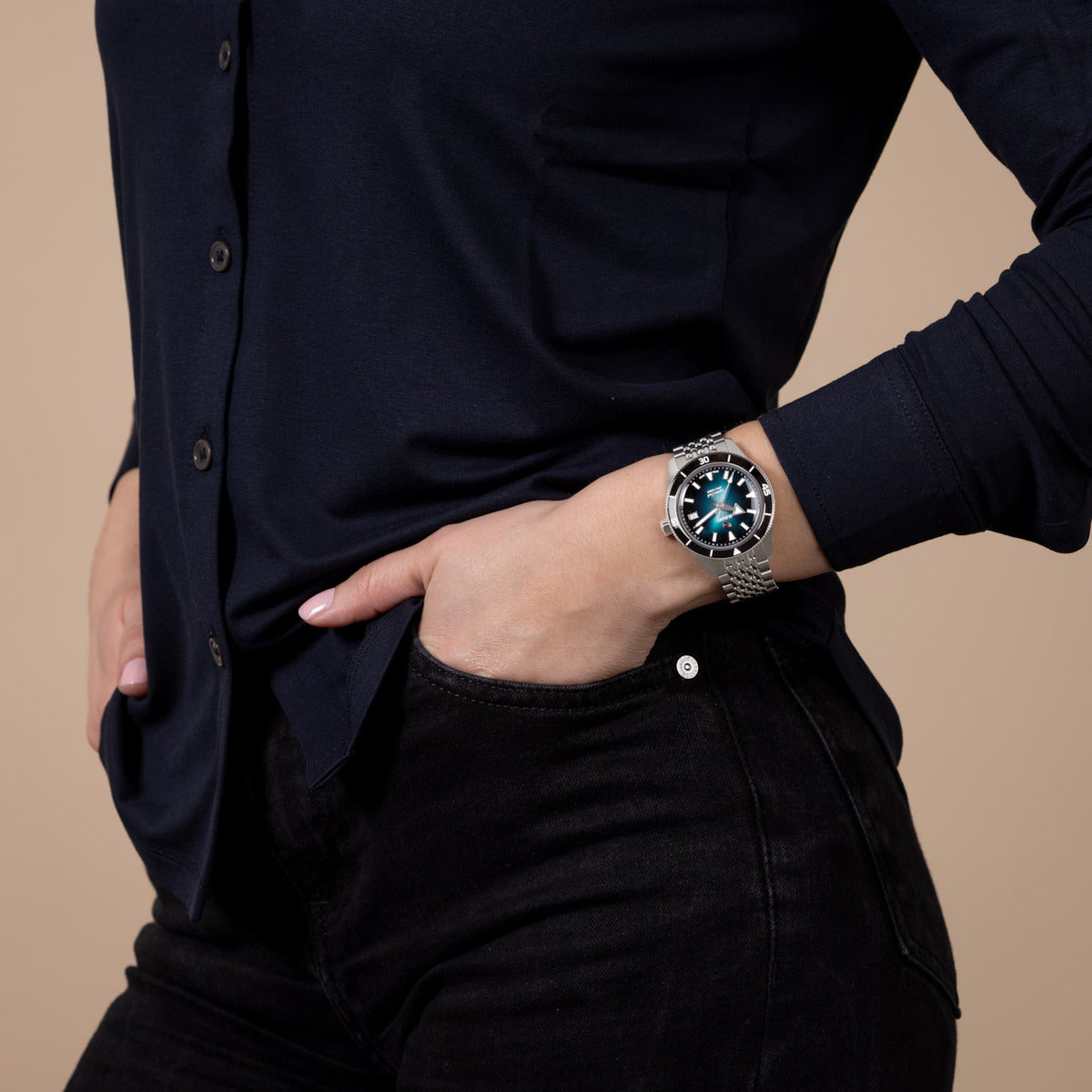 Person wearing a black shirt and dark pants with a watch on a beige background