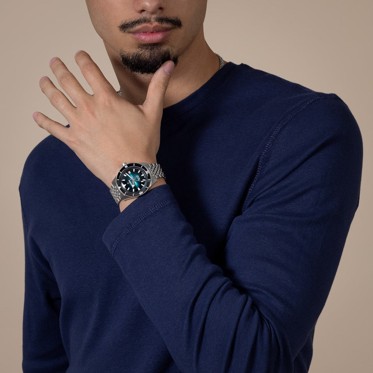 Man wearing a navy blue long-sleeve shirt with a watch on his wrist against a beige background