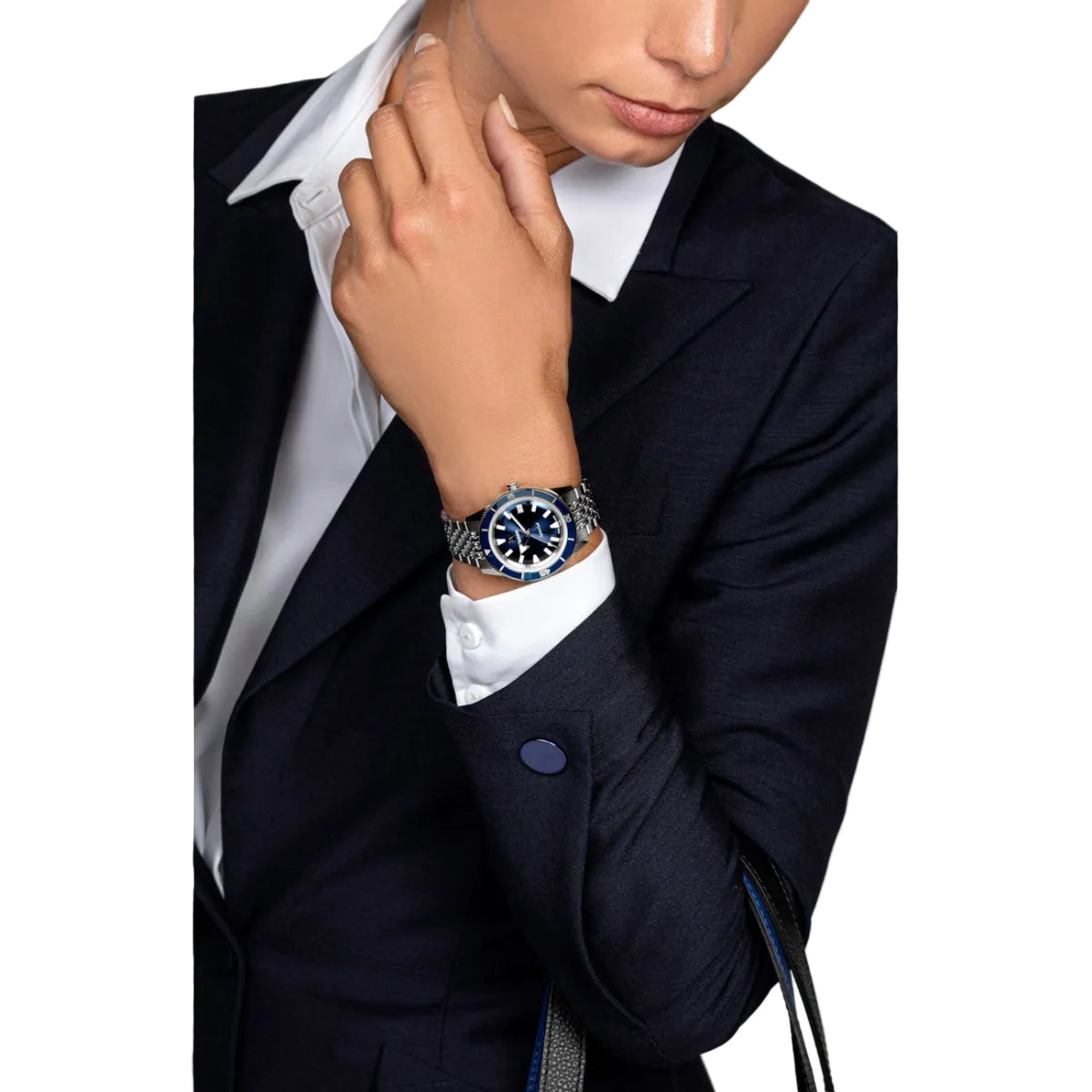 Person wearing a dark suit and white shirt with a watch on a gray background