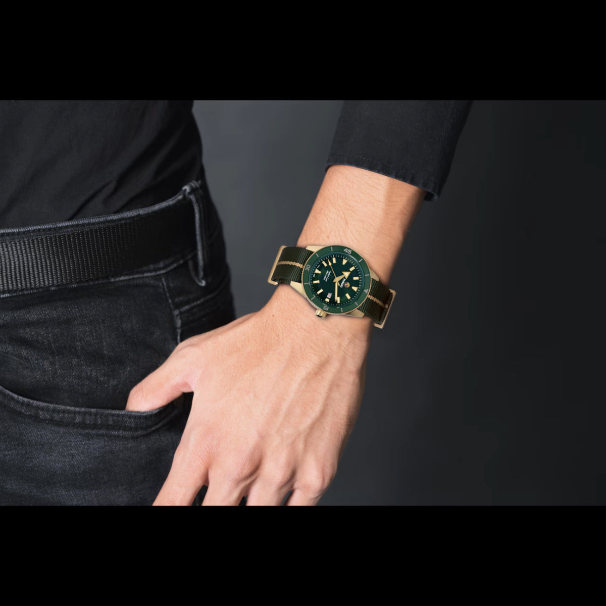 Hand wearing a watch with a green face and gold strap on a dark background
