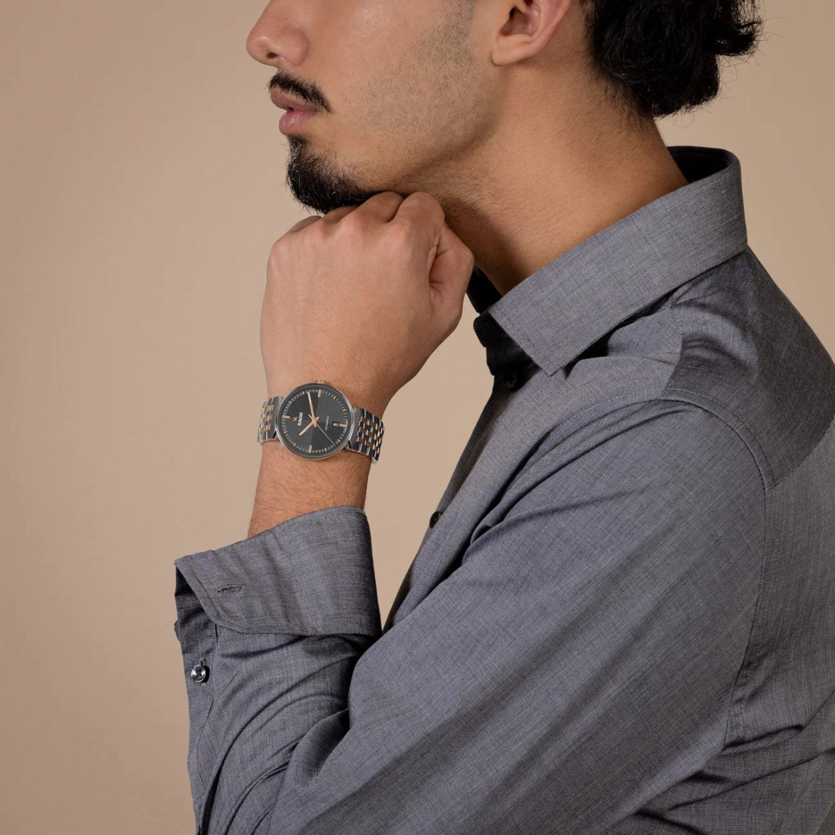 Man wearing a gray suit and patterned watch on a beige background