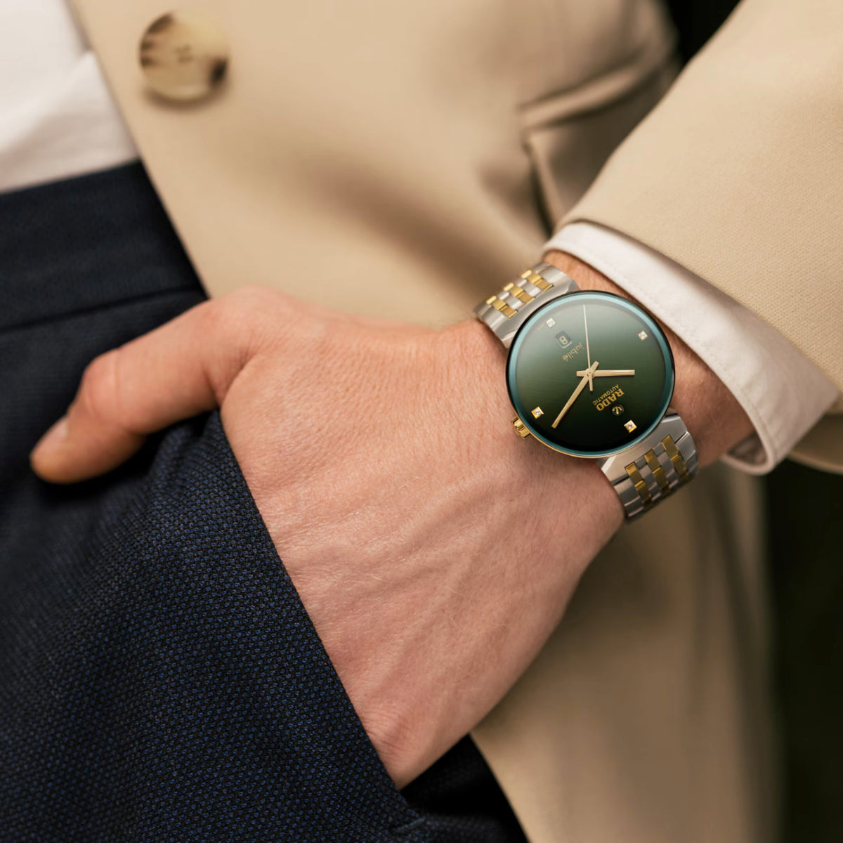 Close-up of a wrist wearing a watch with a green face and gold accents, dressed in formal attire.