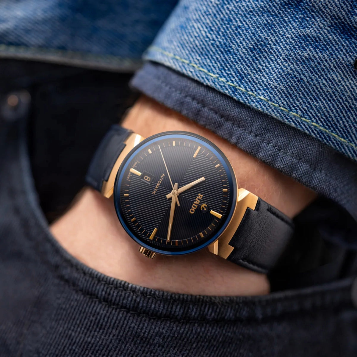 Black and gold watch on a person's wrist with denim background