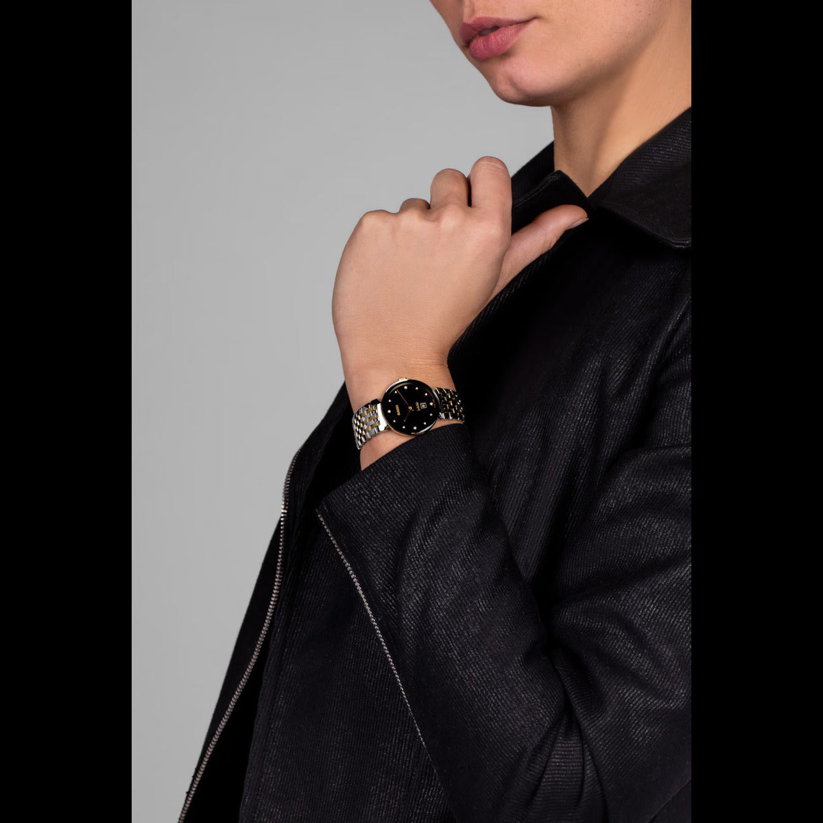 Person wearing a black jacket and a watch on a gray background