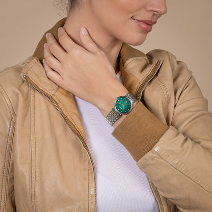 Person wearing a beige jacket and a watch with a green face on a beige background