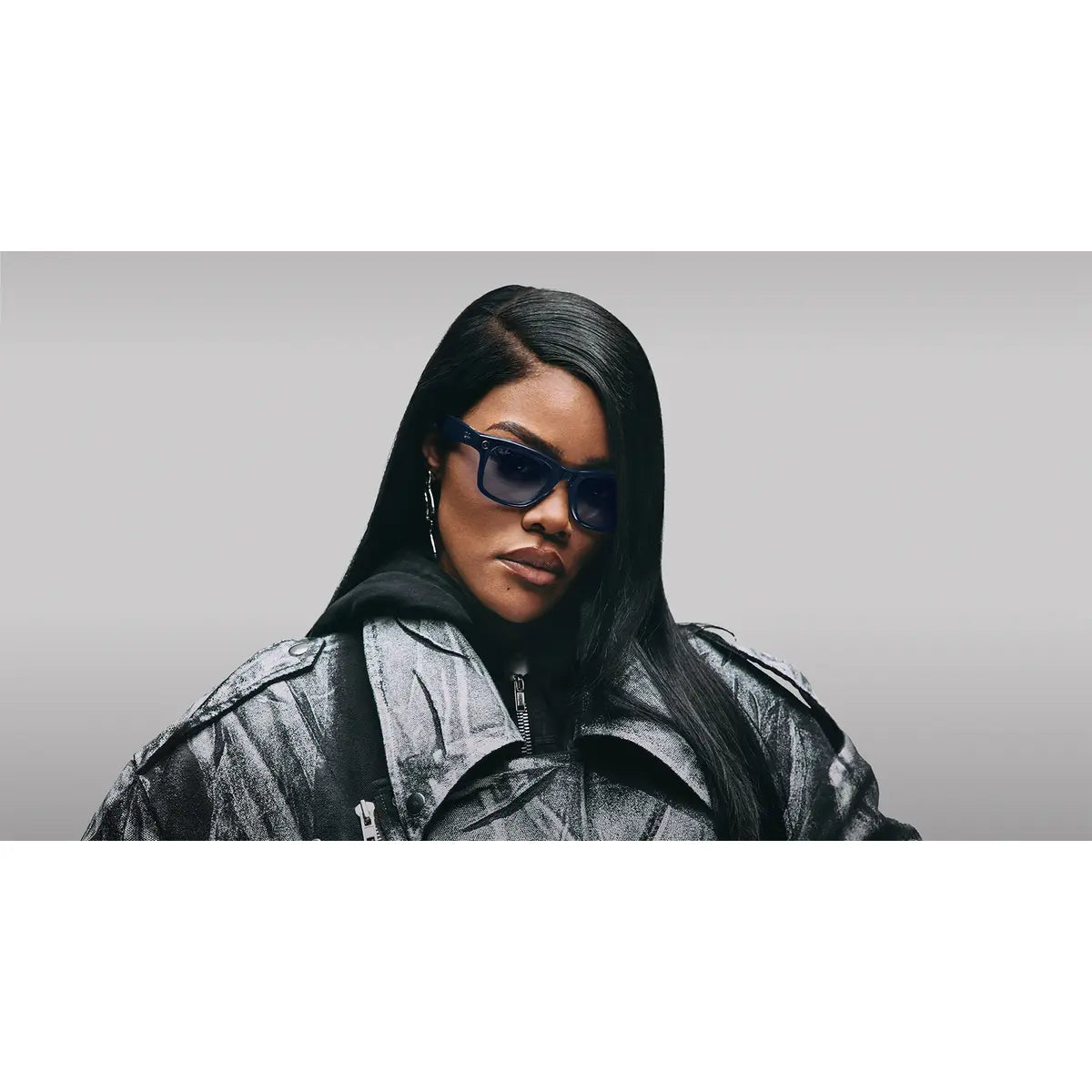 Person wearing a black jacket and blue sunglasses against a gray background