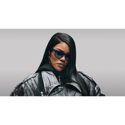Person wearing a black jacket and blue sunglasses against a gray background