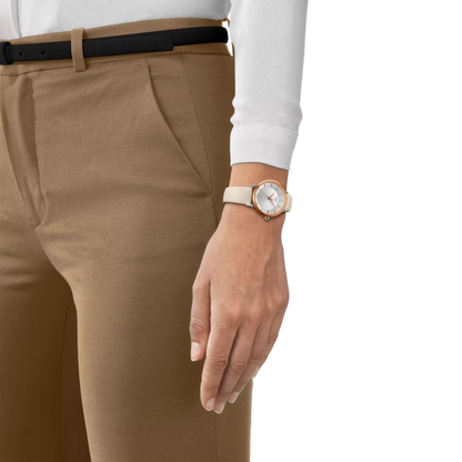 Person wearing beige pants and a white shirt with a watch on a plain background