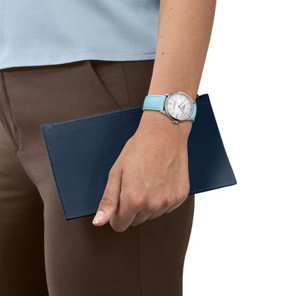 Hand holding a blue clutch with a watch on a white background