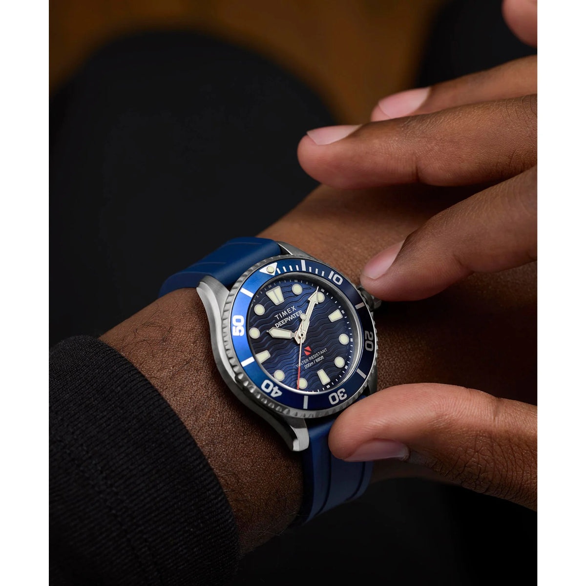 Blue wristwatch with a dark blue face on a person's wrist.