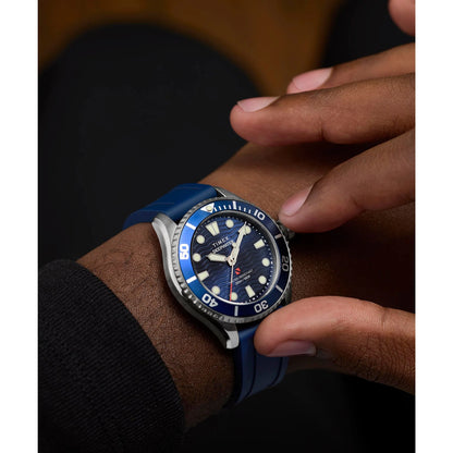 Blue wristwatch with a dark blue face on a person's wrist.