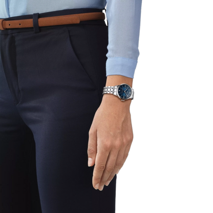 Hand wearing a watch with navy pants and light blue shirt on a white background