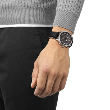 Hand wearing a black watch with a gray sweater and black pants on a white background