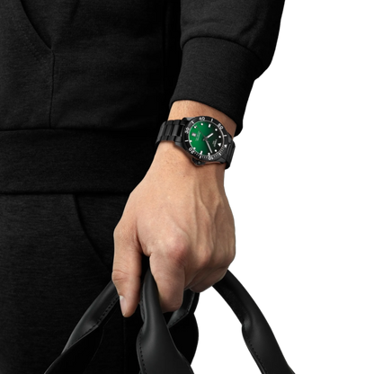 Hand wearing a black watch with a green face, holding a black leather strap.