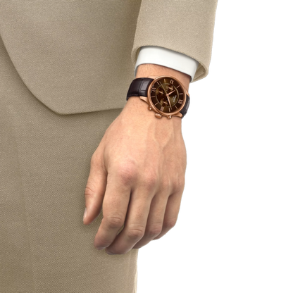 Hand wearing a watch with a detailed face, dressed in a beige suit on a white background