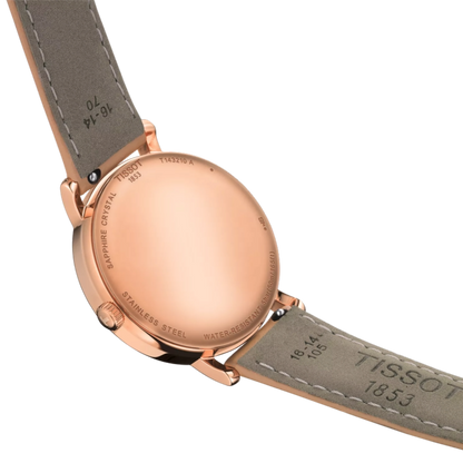 Close-up of a Tissot watch with rose gold case and gray leather strap on a white background