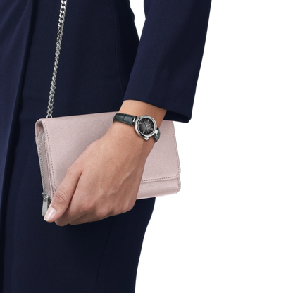 Hand holding a pink clutch with a chain strap, wearing a dark watch, against a white background.