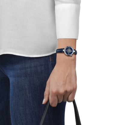Person wearing a watch with a white shirt and blue jeans on a plain background