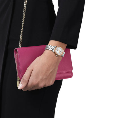 Hand holding a pink clutch with a watch on a white background