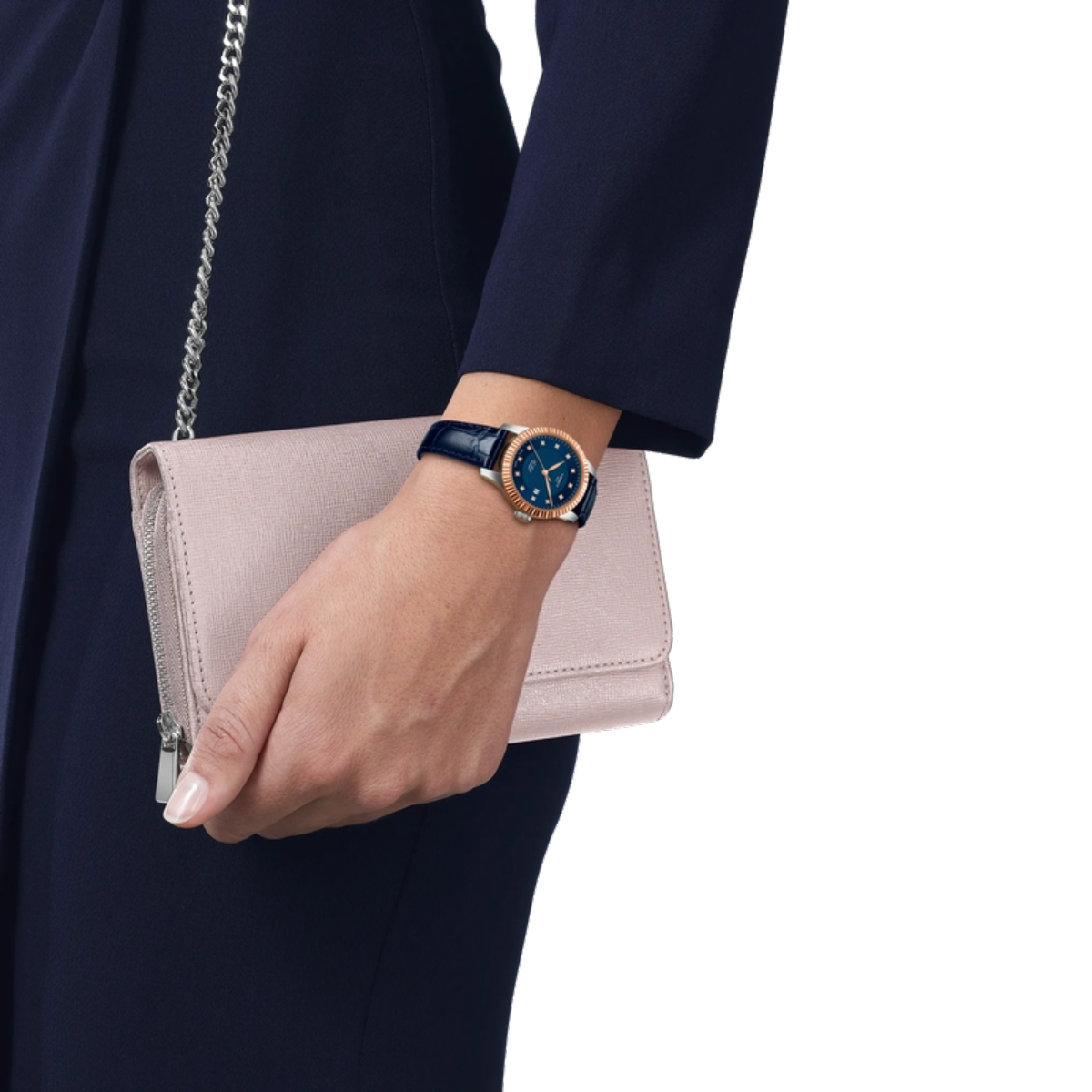 Hand holding a light pink clutch with a person wearing a dark blue watch on a white background