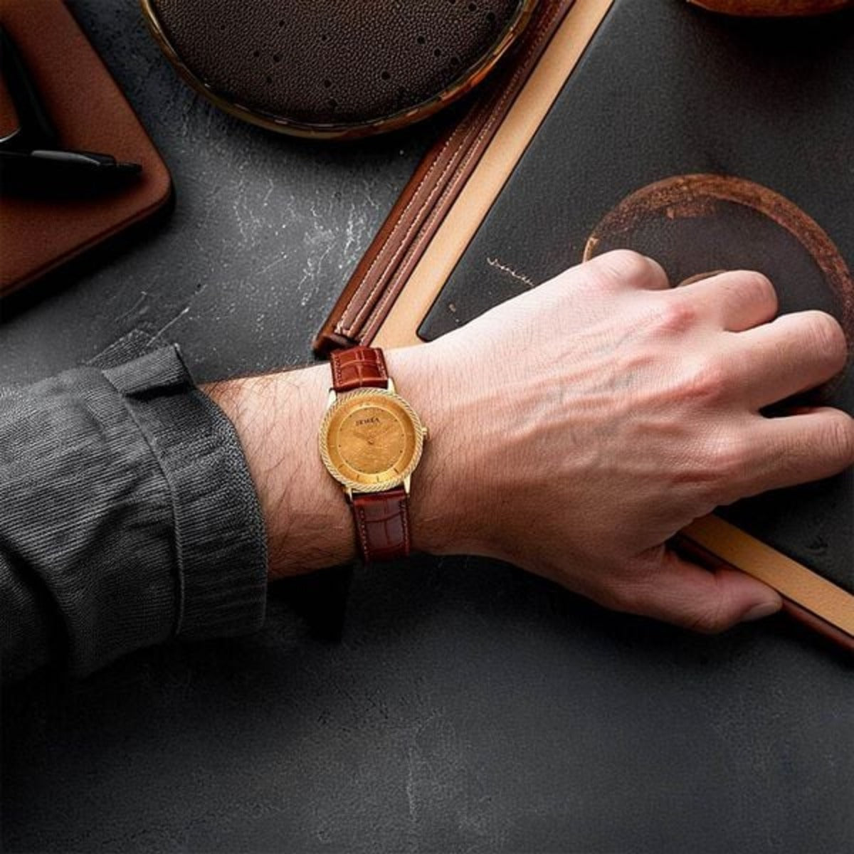 Hand wearing a gold watch with a brown leather strap on a dark surface