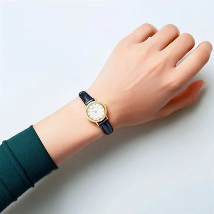 Hand wearing a watch with a blue strap on a light gray background