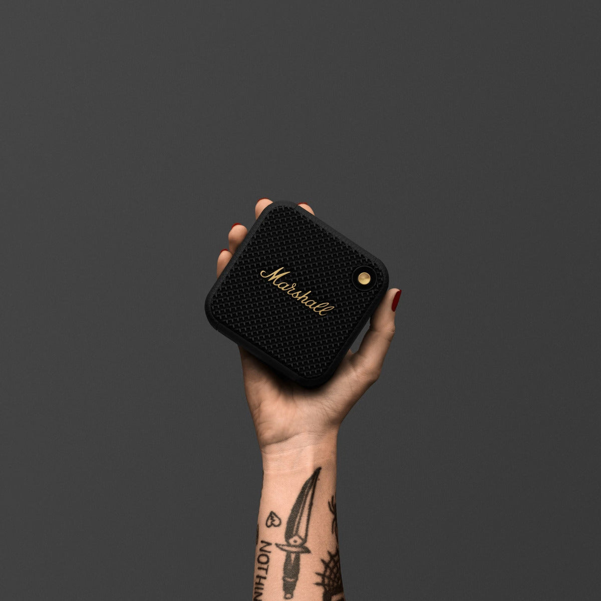 Hand holding a Marshall speaker against a dark background
