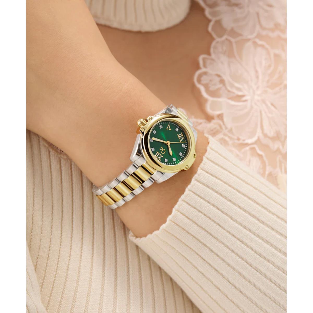 Gold and silver watch with green face on a wrist against a neutral background